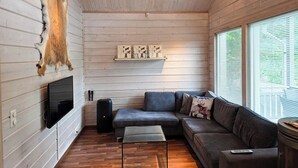 A cozy cabin interior with a wooden ceiling, a mounted television, a sofa, and a window with blinds. - Villa Chalet, Himos Länsihuippu (Jämsä)