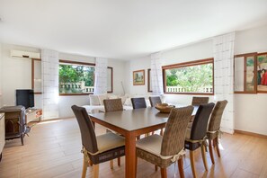 A dining area with a wooden table and wicker chairs, a television, and a view of greenery outside. - Mallorcan Villa with Pool in S'Amarador (Santanyí)
