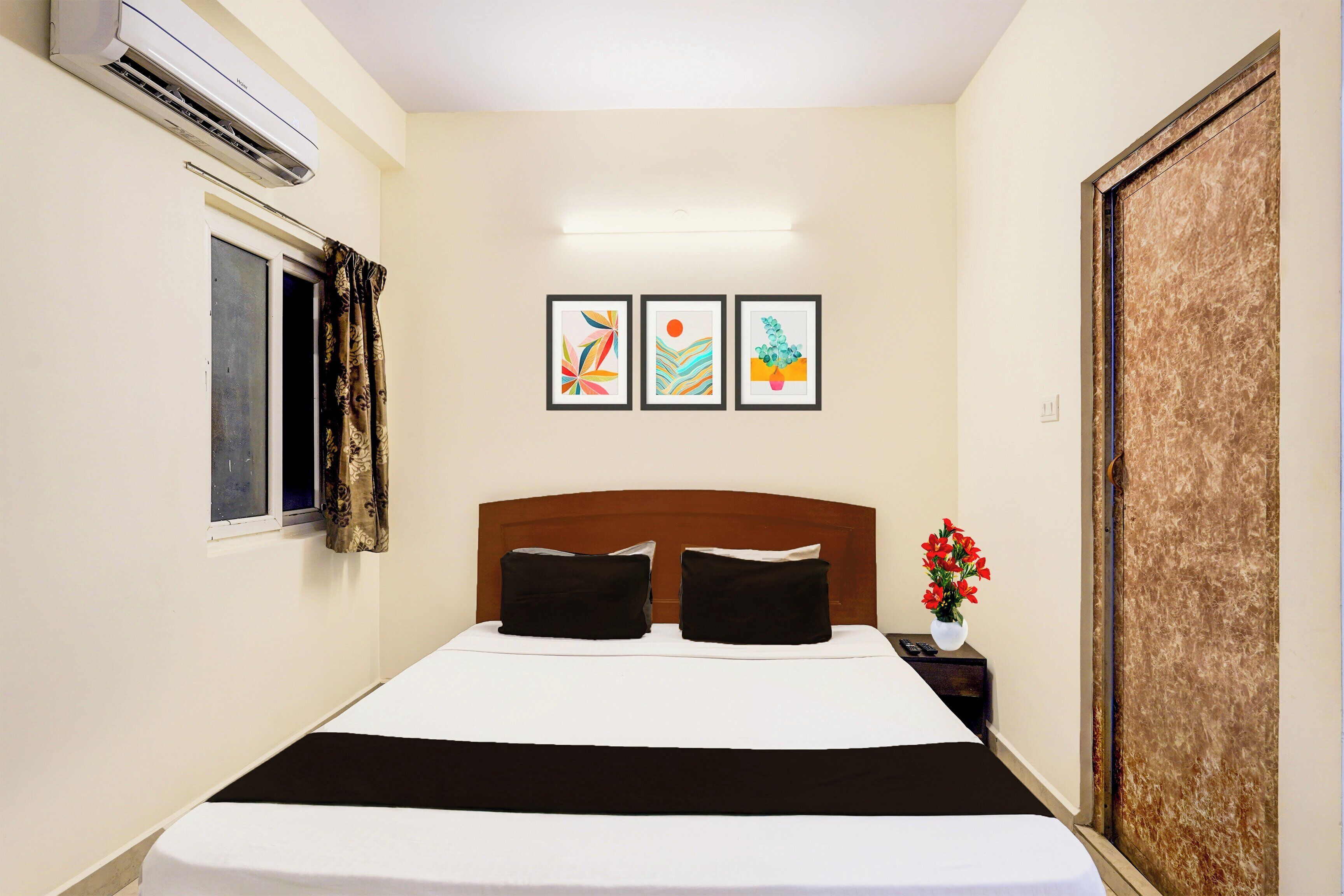 Habitación de hotel con cama, mesita de noche, planta en maceta y tres cuadros en la pared.