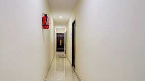 Un pasillo con un extintor montado en la pared, una puerta al final y suelo de baldosas.