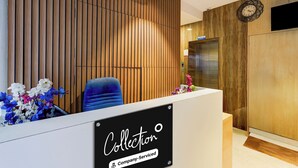 Una recepción con un cartel que dice 'Collector Company-Serviced', una silla azul, un reloj y un ascensor.