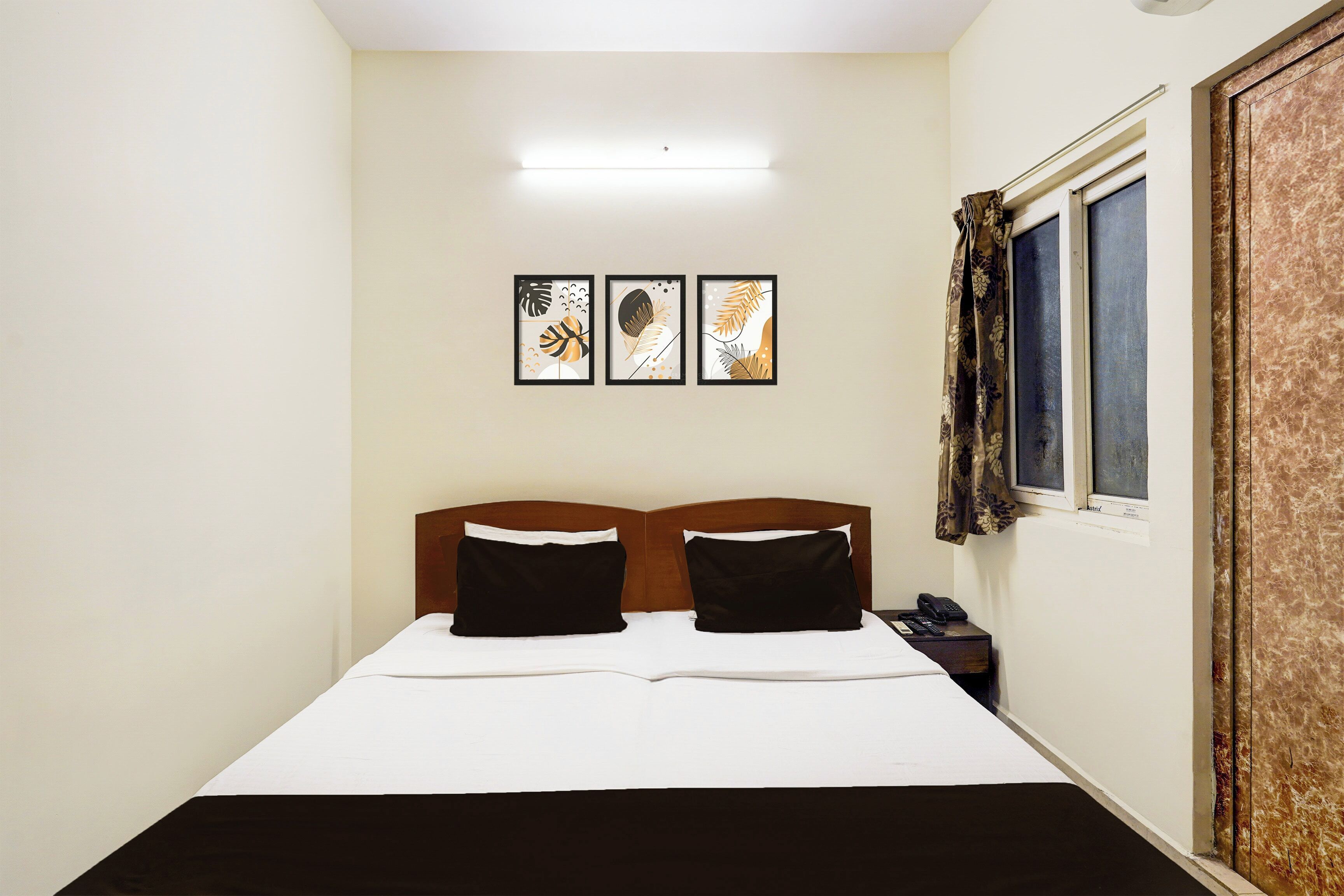 Habitació d'hotel amb un llit, dos coixins negres, una taula de nit amb un telèfon i tres quadres penjats a la paret.