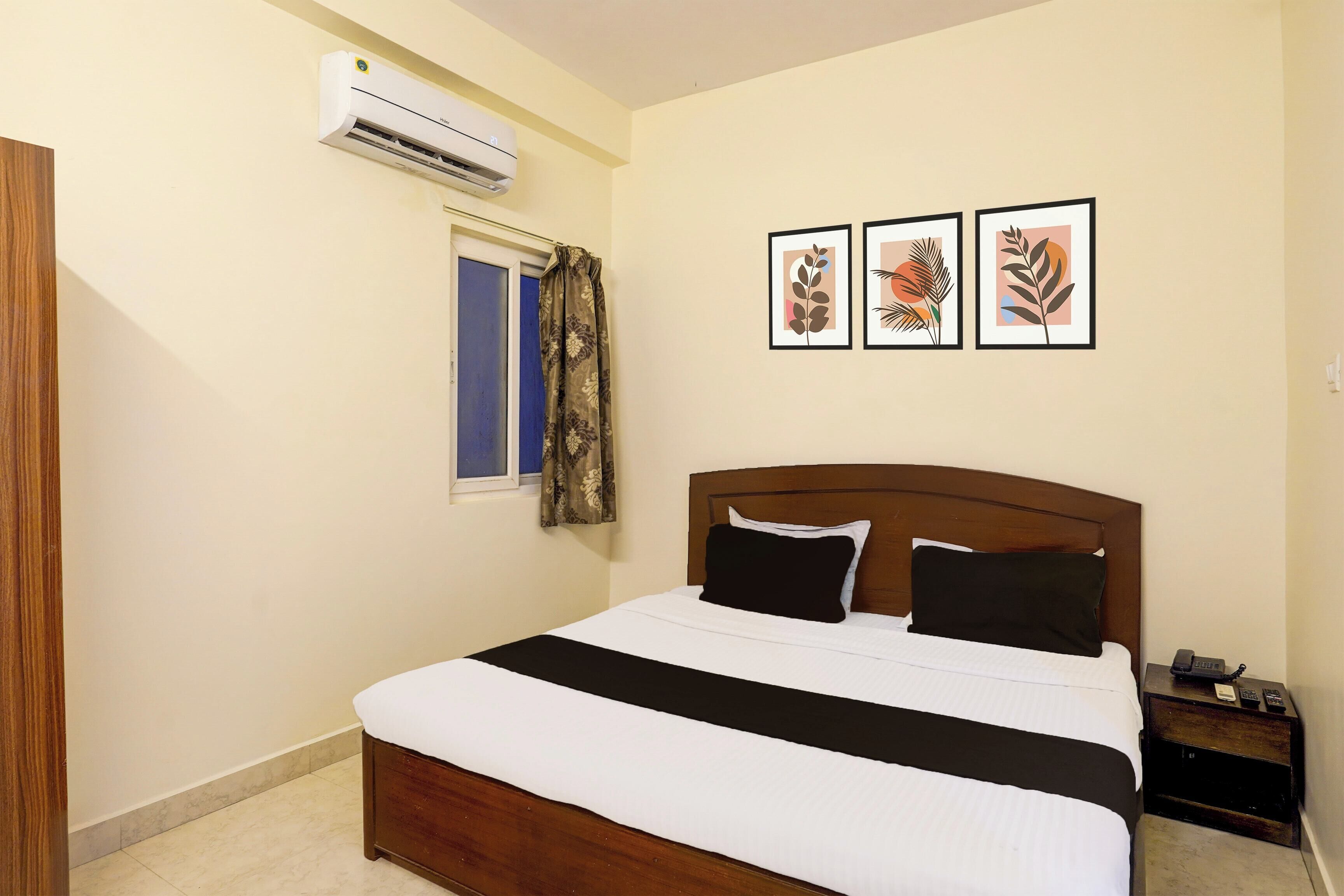 A bedroom with a bed, an air conditioning unit, a window with curtains, and three framed pictures on the wall.