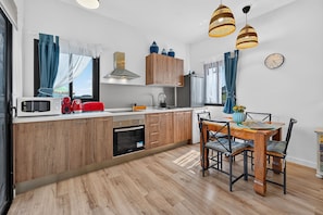A modern kitchen with wooden cabinets, a built-in oven, a microwave, and a dining area with a table and chairs. - Vacation studio for 3 people in La Laguna (La Vega)