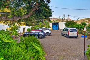 A gravel driveway with two cars parked, surrounded by greenery and a building with a blue door. - Vacation studio for 3 people in La Laguna (La Vega)