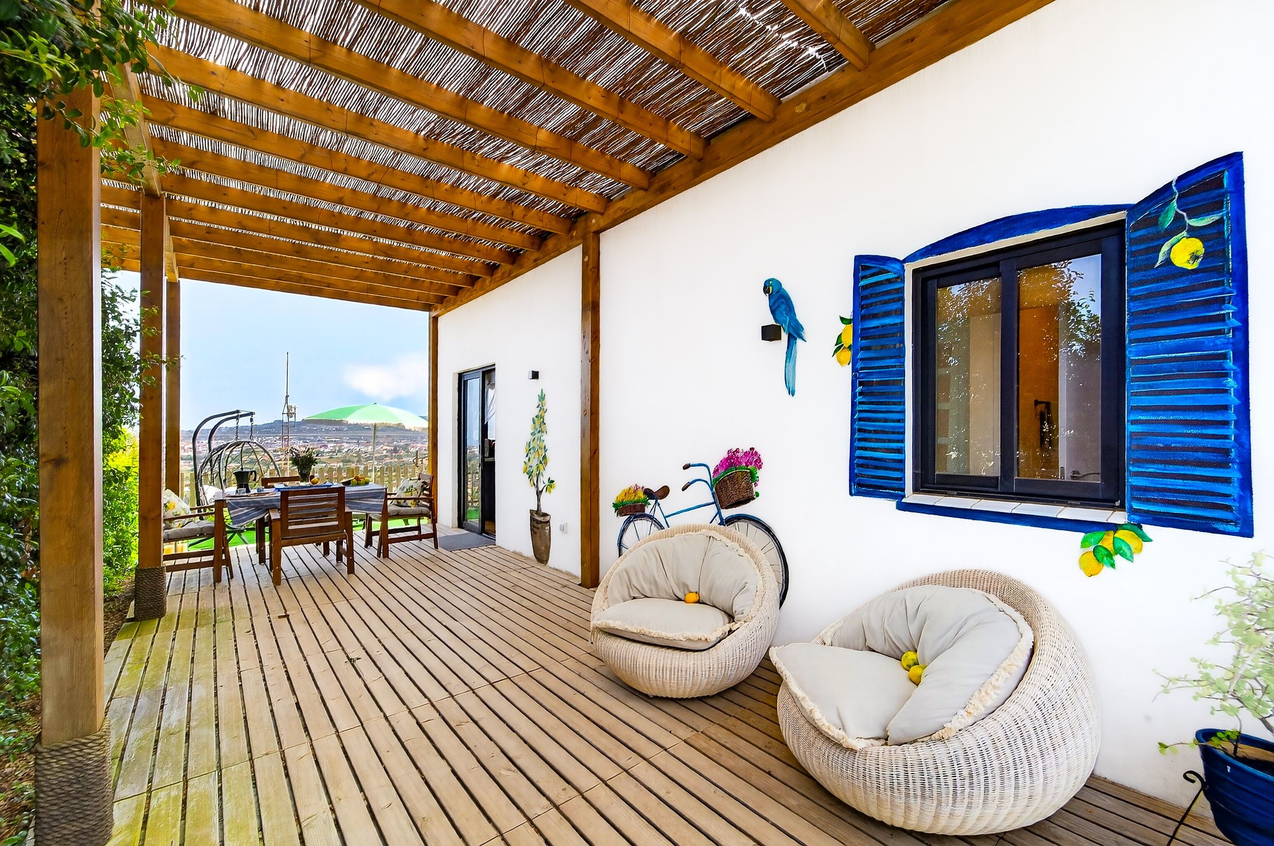 A covered outdoor seating area with wooden flooring, wicker chairs, and a view of the cityscape.