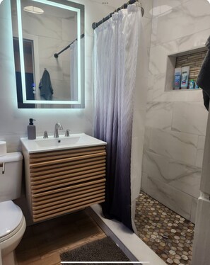 Ein modernes Badezimmer mit Waschtisch, Toilette, Duschkabine und Spiegel.