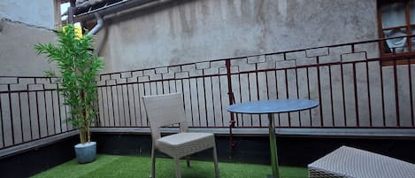 A courtyard with artificial grass, a table, two chairs, and a potted plant.