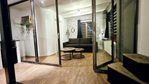 A modern living room with a sofa, a coffee table, and a glass door leading to another room. - L'ECRIN VERT  (Kaysersberg-Vignoble)