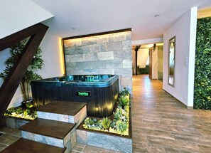 Un moderno espacio de spa con pared de piedra, una bañera de hidromasaje y una escalera con jardín.