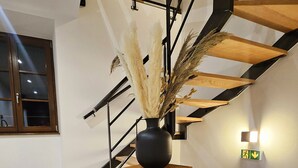 A modern staircase with a wooden finish, a black vase with dried plants, and a wall-mounted light fixture. - L'ECRIN VERT  (Kaysersberg-Vignoble)