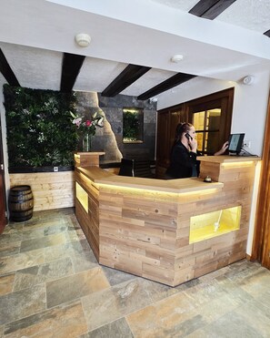 Una recepción con detalles de madera, una pared de piedra con plantas y un suelo de baldosas.
