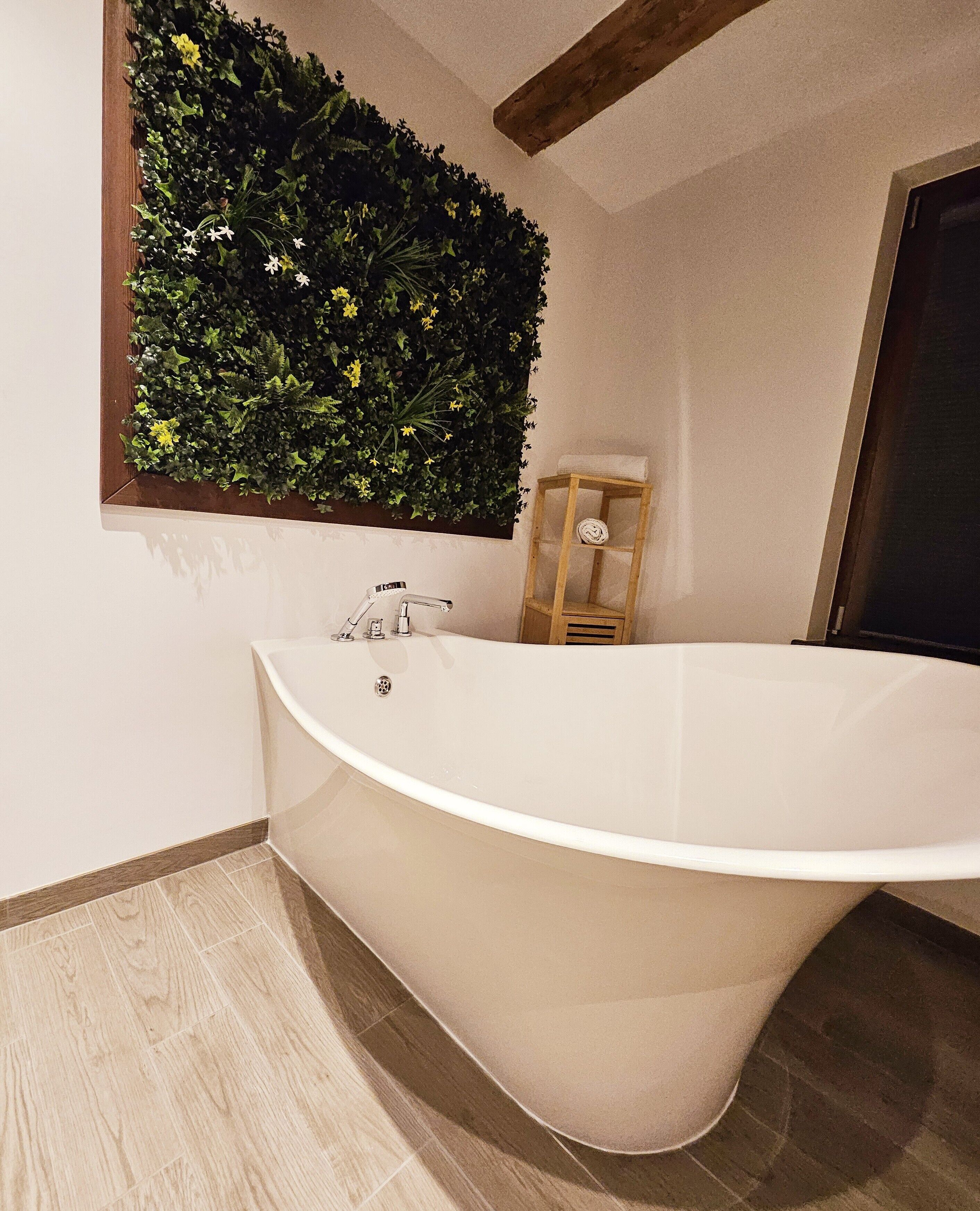 A modern bathroom with a freestanding bathtub, a wooden shelf with a towel, and a wall-mounted green plant.