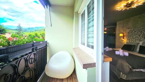 A balcony with a view of a green landscape, a white chair, and a bed with pillows and a lamp. - L'ECRIN VERT  (Kaysersberg-Vignoble)