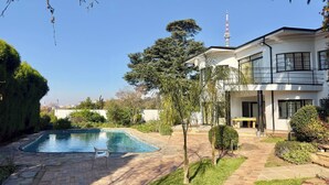 A modern two-story house with a swimming pool, a balcony, and a view of a tall tower. - Room-double Self-contained Room 6 (Johannesburg)