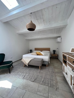Ein Schlafzimmer mit einem Bett, Nachttischen, einer Hängelampe, einem Sessel und einer Kommode.