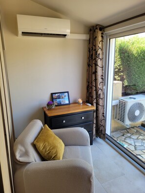 A room with a sofa, a small table with a picture frame and candle, and an air conditioning unit.