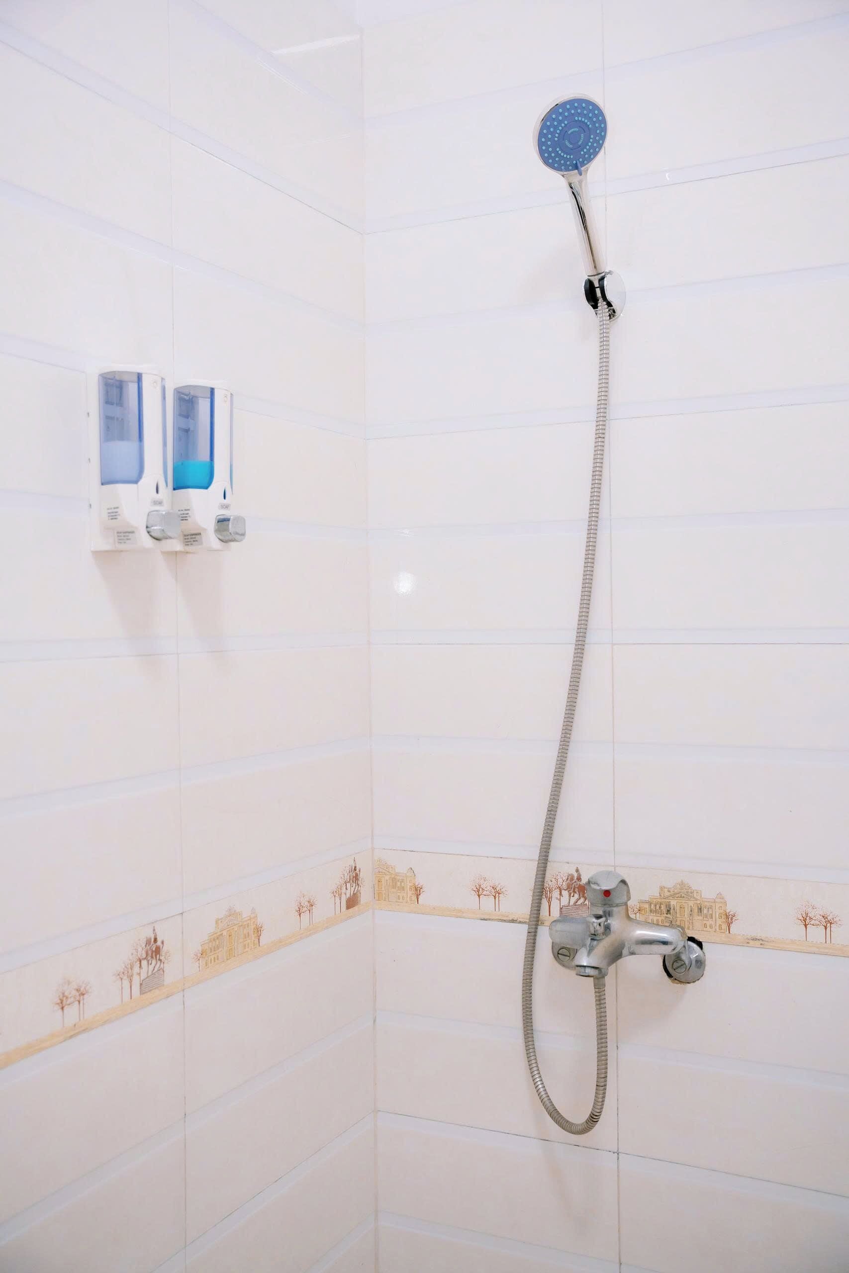 Une douche équipée d’un pommeau de douche à main et d’un robinet mural. Deux distributeurs de savon sont fixés au mur.