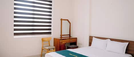 A hotel room with a bed, a wooden nightstand, a mirror, a chair, and a window with blinds.