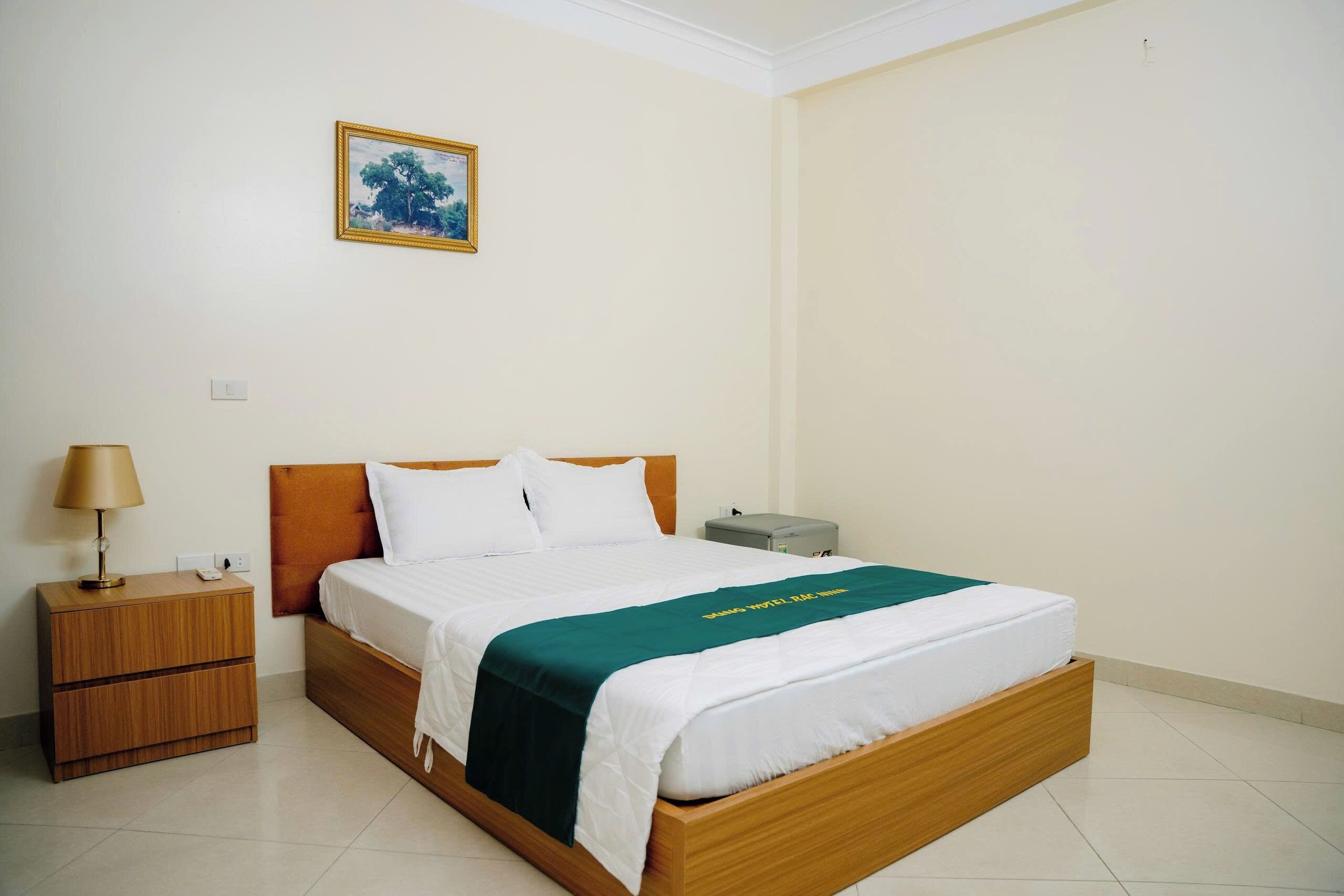 A hotel room with a bed, a nightstand, a lamp, a power outlet, and a picture on the wall.