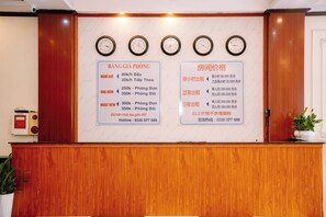 A reception desk with a marble wall, four clocks, and two informational signs in a foreign language. - Lotus Hotel 1 (Hap Linh)