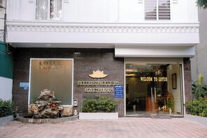 The exterior of a hotel with a large sign reading 'LOTUS HOTEL' and a welcome sign. There is a small rock garden with a water feature in front. - Lotus Hotel 1 (Hap Linh)