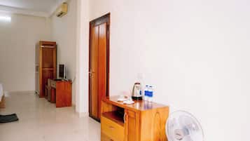 Habitación de hotel con armario de madera, escritorio con hervidor, ventilador y televisor.