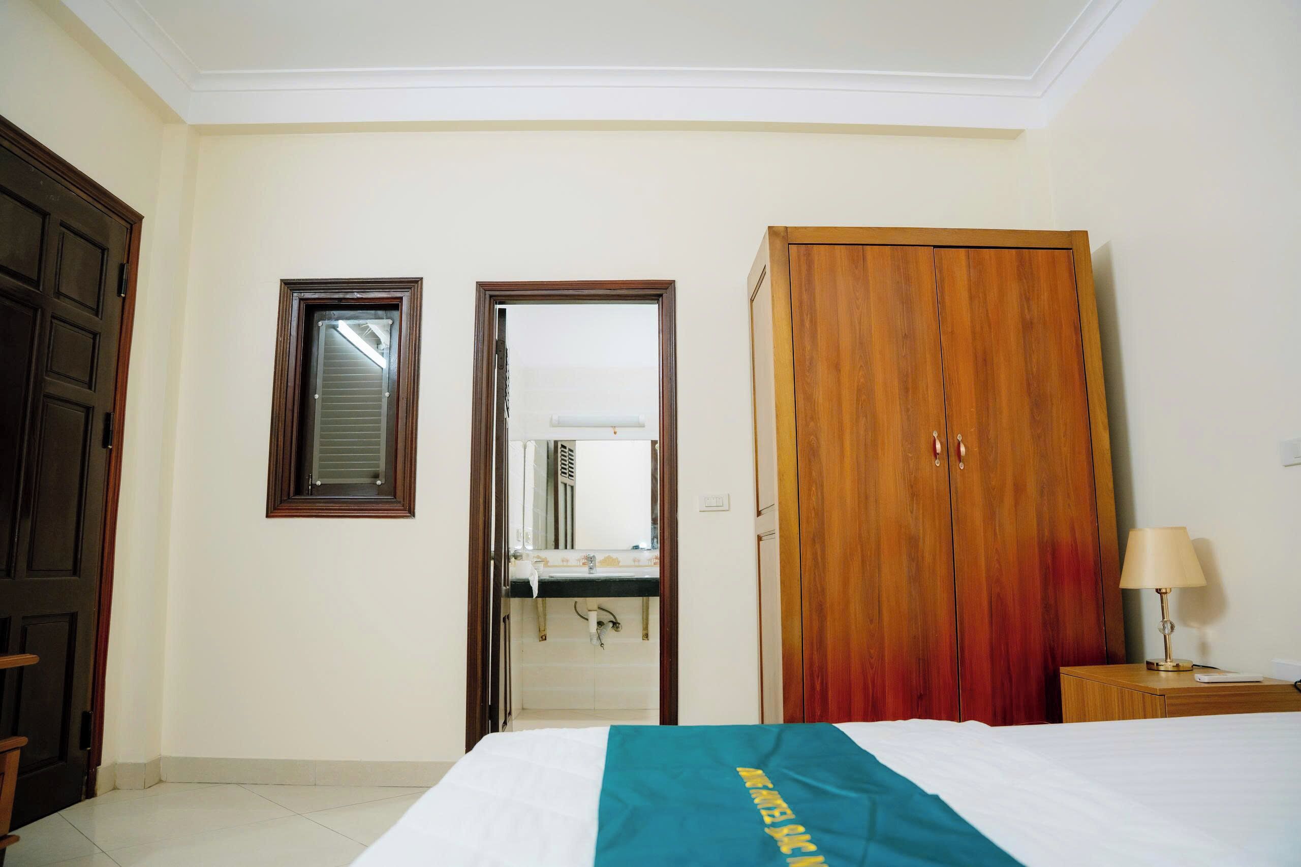 A hotel room with a bed, a wardrobe, a mirror, and a door leading to a bathroom.