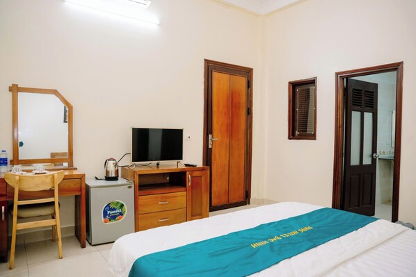 Habitación de hotel con cama, escritorio, silla, televisor, armario y puerta de baño.