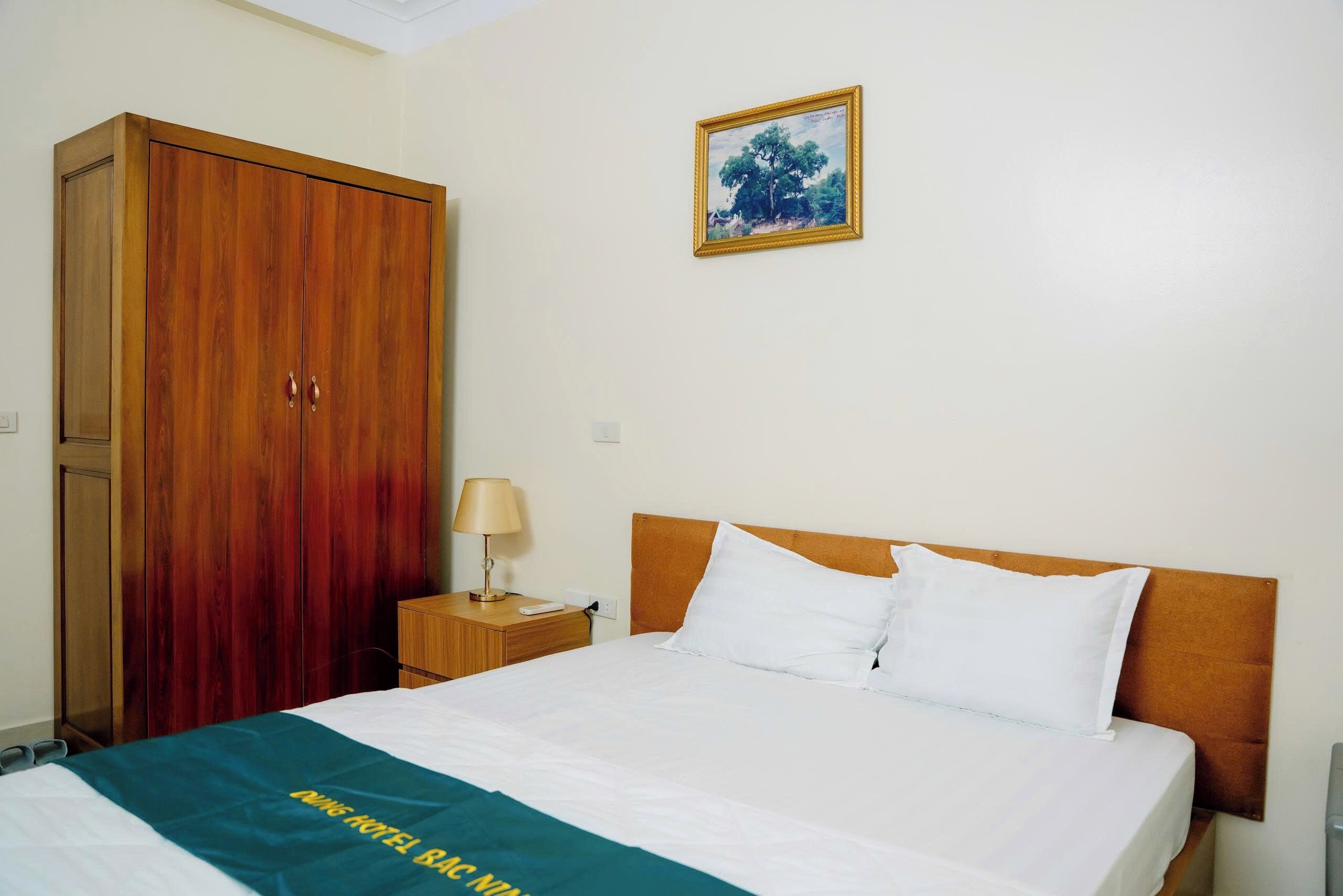Une chambre d’hôtel avec un lit, une armoire en bois, une table de chevet avec une lampe et un tableau encadré au mur.