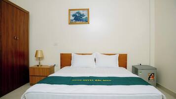 A hotel room with a bed, a nightstand, a lamp, a picture on the wall, and a water dispenser.