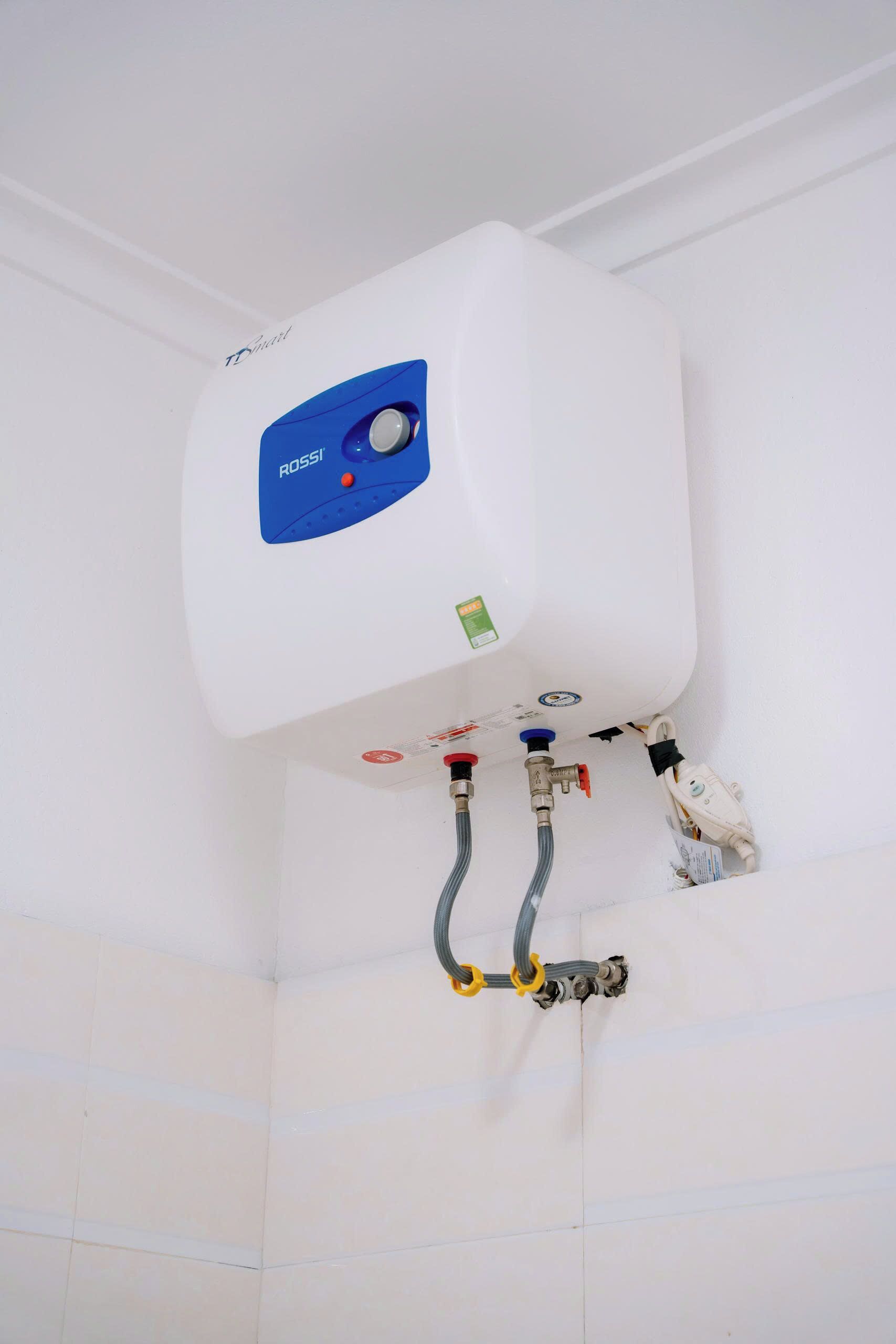 A white water heater with a blue control panel, connected to a wall with white tiles.