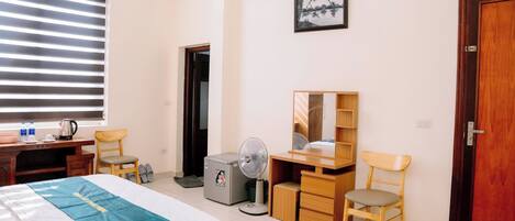 Quarto de hotel com duas camas, uma escrivaninha, uma cadeira, um ventilador, um guarda-roupa e um quadro na parede.