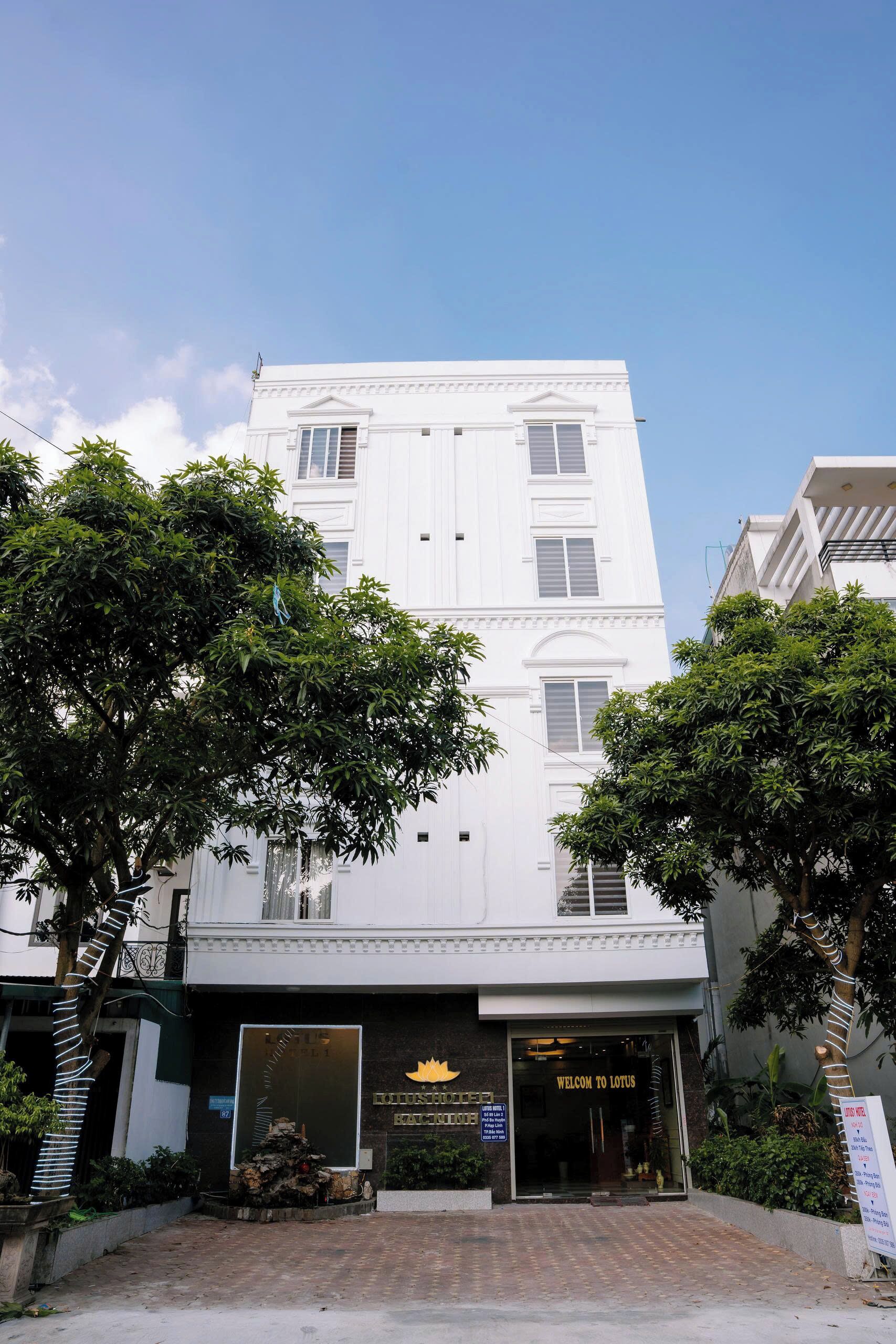 Un hotel de varios pisos con fachada blanca, un cartel con el nombre Hotel Lotus y una entrada acogedora.