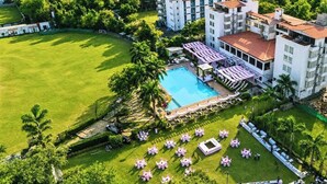 A hotel with a swimming pool, outdoor seating, and a well-maintained lawn. - Presidency Club Resort & Spa  (Vadodara)