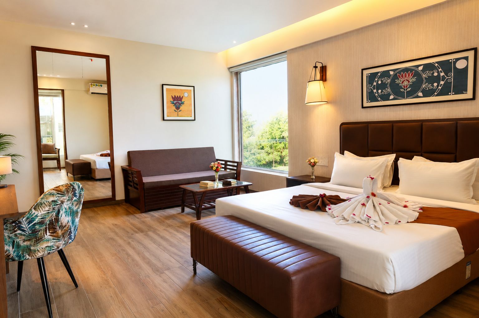 Habitación de hotel con una cama grande, un sofá, una mesita, una silla y una ventana con vistas a la vegetación.