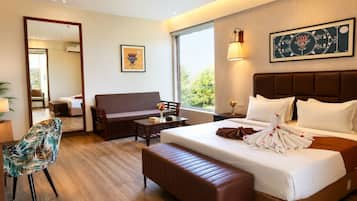 Habitación de hotel con una cama grande, un sofá, una mesita, una silla y una ventana con vistas a la vegetación.