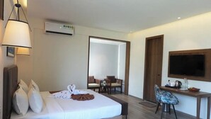 A hotel room with a bed, bedside table, lamp, desk with chair, TV, and a mirror. - Presidency Club Resort & Spa  (Vadodara)