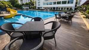 A pool area with a yellow slide, wicker furniture, and a modern building in the background.