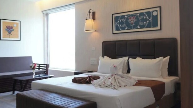 A modern hotel room with a large bed, a bedside table, a chair, a desk, and a window. - Presidency Club Resort & Spa  (Vadodara)
