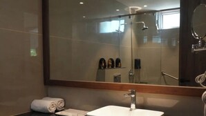 A bathroom with a large mirror, a white sink, and a dark countertop. - Presidency Club Resort & Spa  (Vadodara)