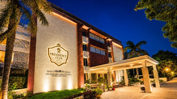 A hotel with a prominent 'Presidency Club' sign, a covered entrance, and a well-lit facade.