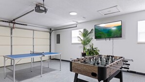 A room with a ping pong table, a foosball table, a television, and a plant. - Noir Manor (Sevierville)