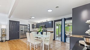 A modern kitchen with a dining area, featuring a refrigerator, microwave, and a glass table with chairs. - Noir Manor (Sevierville)