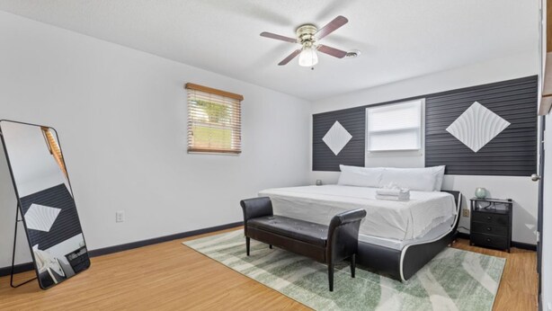A bedroom with a bed, a nightstand, a chair, a ceiling fan, and a window with blinds. - Noir Manor (Sevierville)