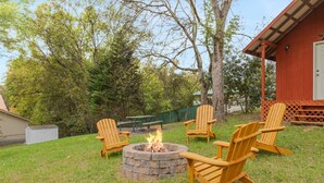 A backyard with a fire pit, four Adirondack chairs, and a red building. - Noir Manor (Sevierville)