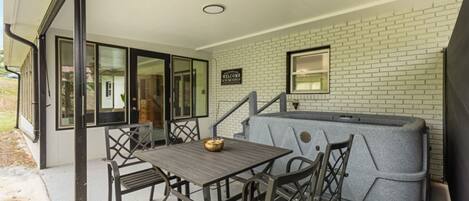 Une terrasse extérieure avec une table et des chaises, un jacuzzi et un mur en briques.