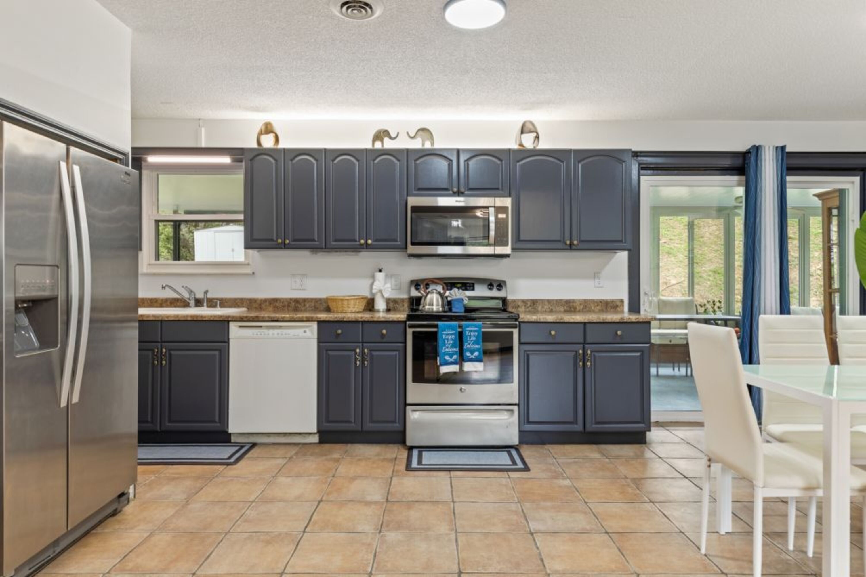 A modern kitchen with dark cabinets, stainless appliances, and a dining area with white chairs.