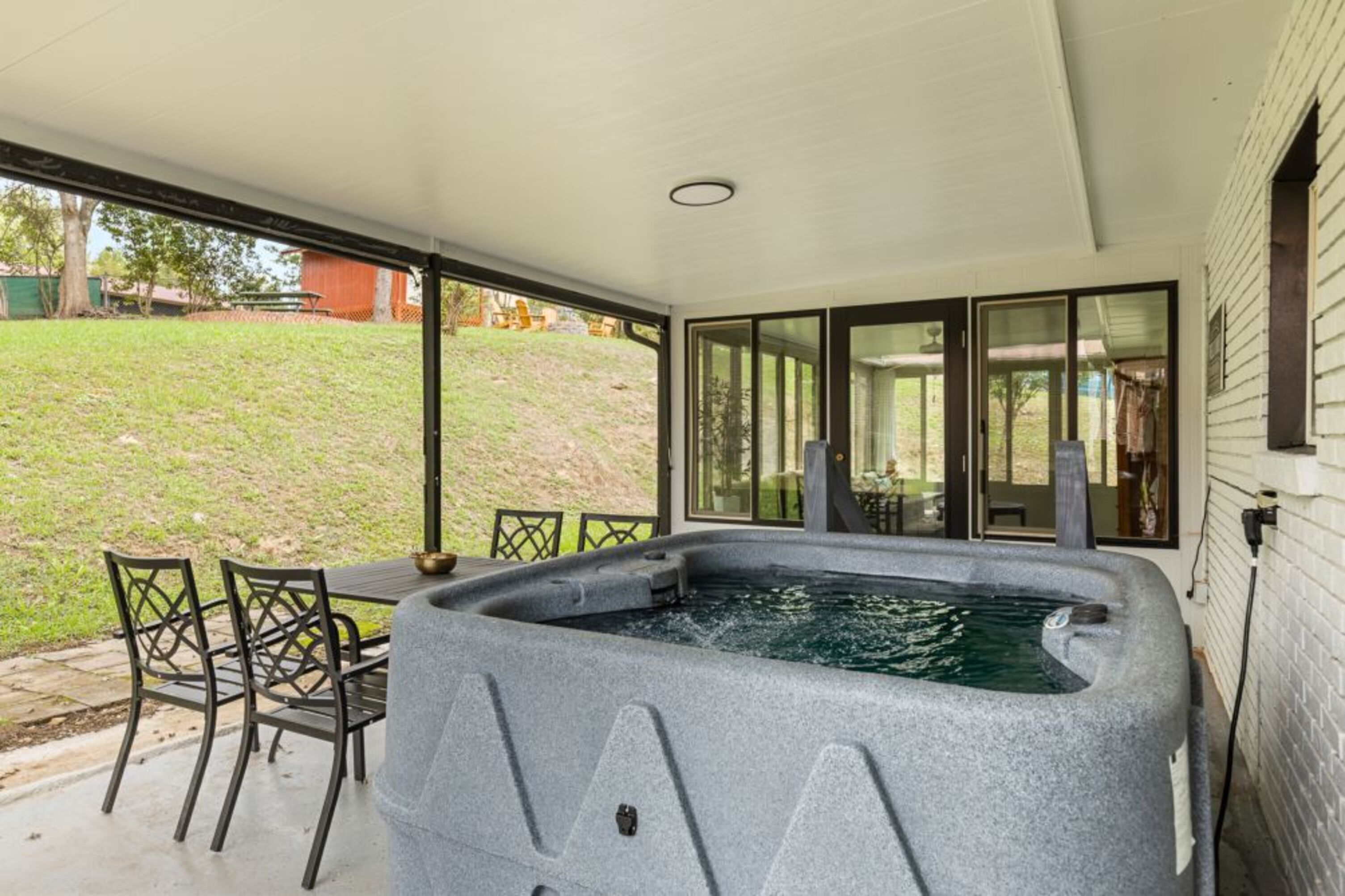 Un jacuzzi con una mesa y sillas frente a una casa con ventanas grandes.
