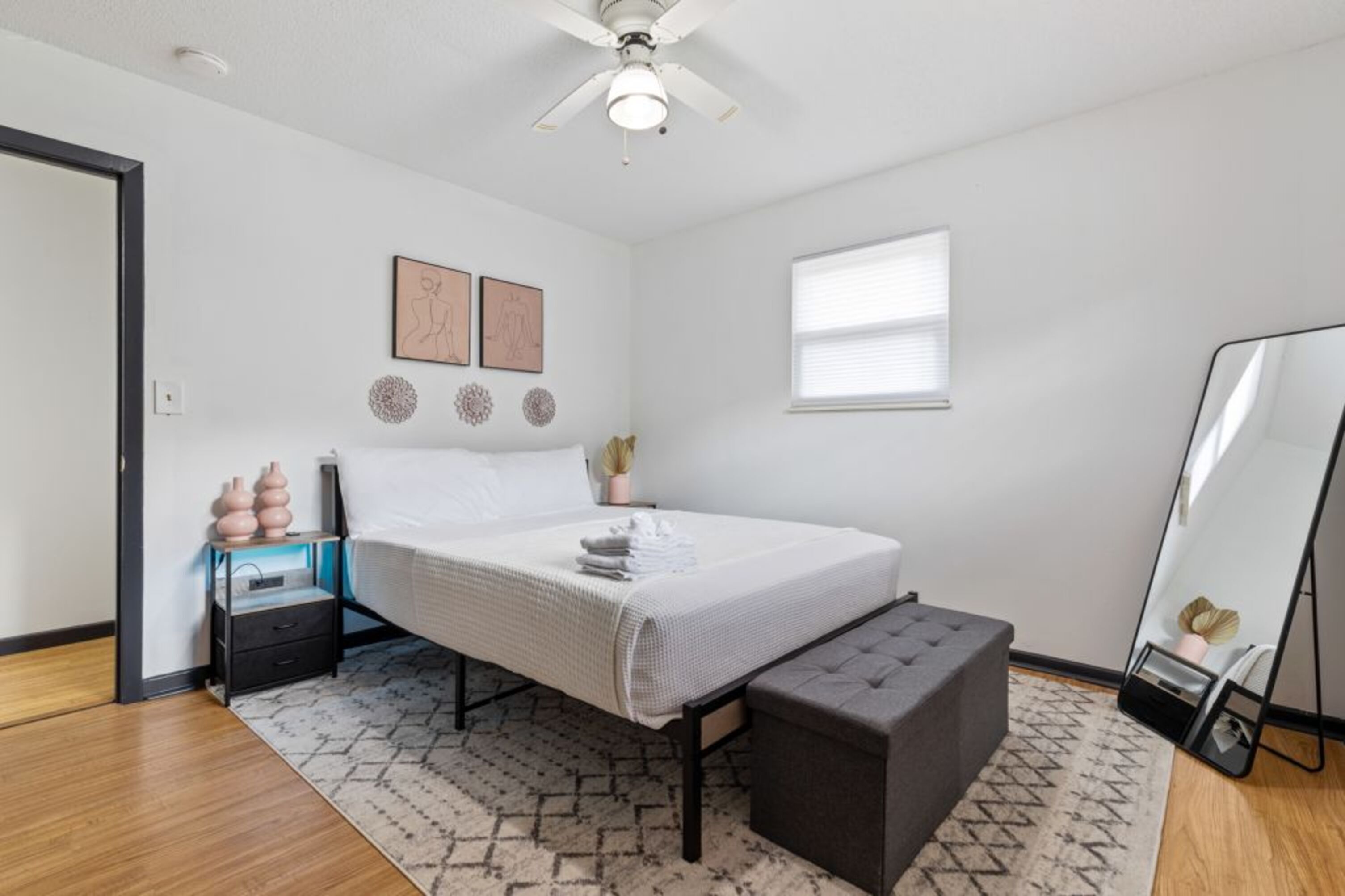 A bedroom with a bed, bedside tables, a mirror, and a ceiling fan.